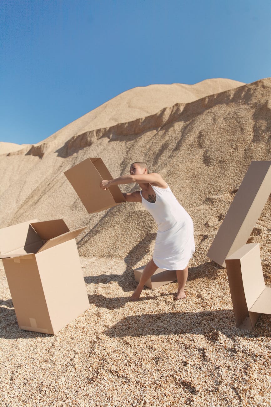 informal young woman carrying carton boxes in desert on sunny day